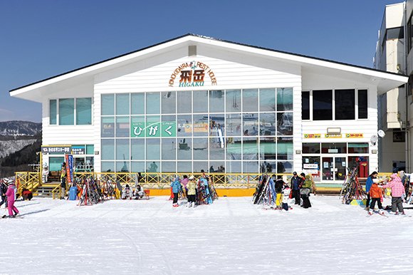 ガラス張りの正面に「飛岳」の看板がある建物と、前に集まるスキー客