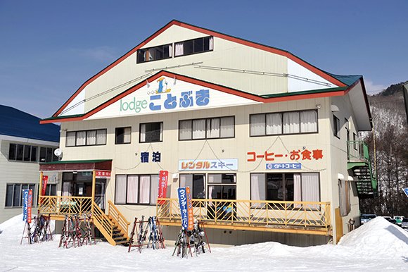 赤い屋根縁の「lodge ことぶき」の建物。前にスキーラック