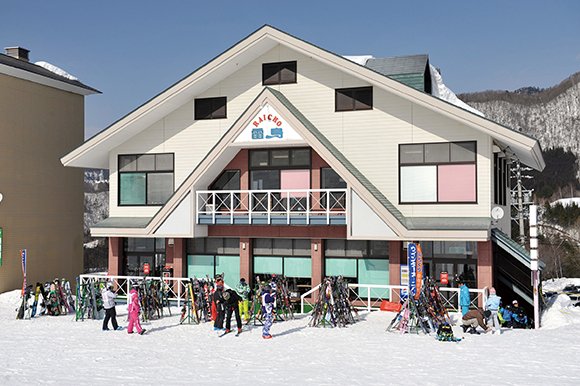 Lodge Raicho exterior: gabled lodge with skiers and ski racks in front