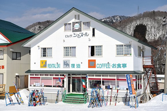 Lodge Spur exterior: white lodge with RENTAL SKI and COFFEE signs, ski racks in front